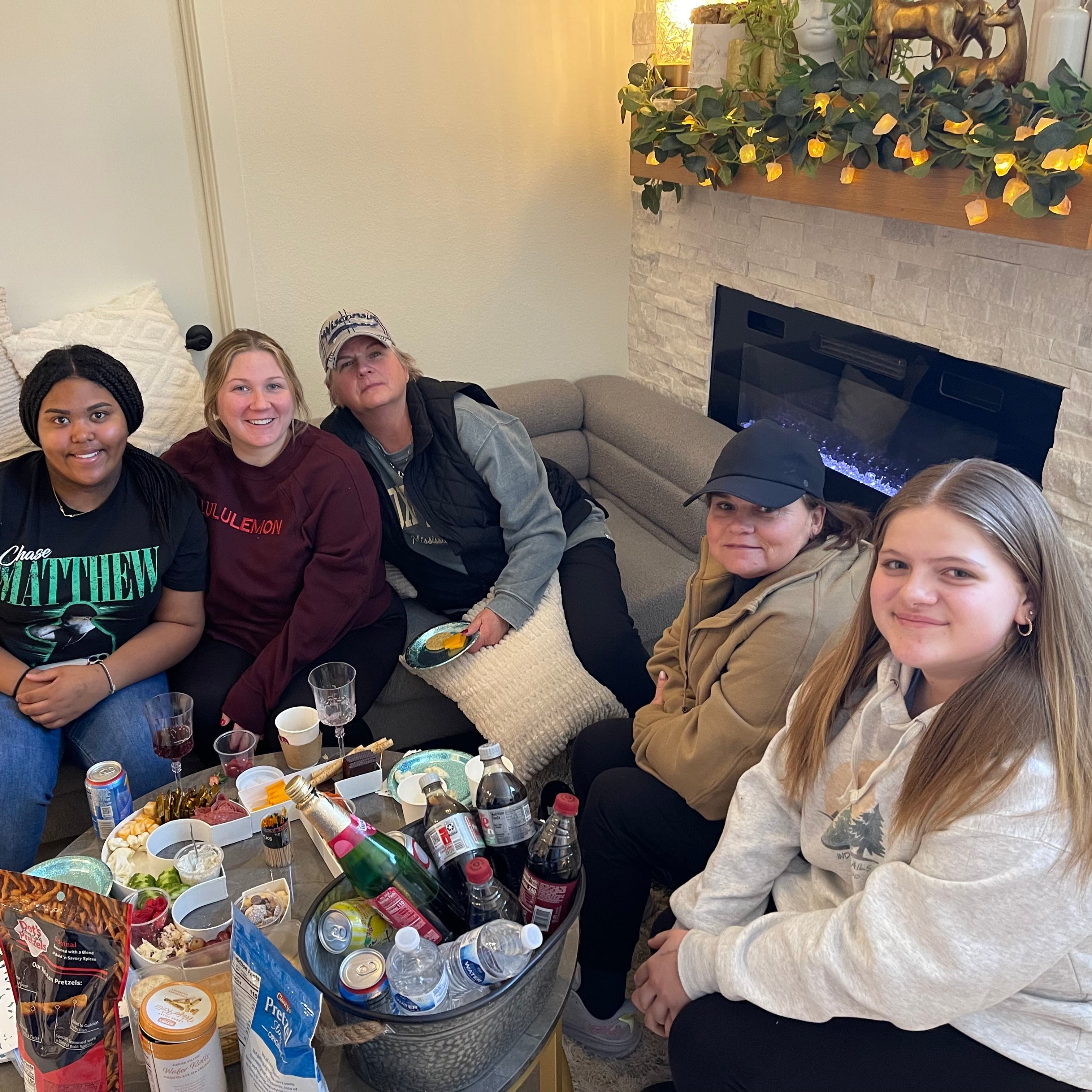 Group of people sitting on a couch in a living room with snacks and drinks.
