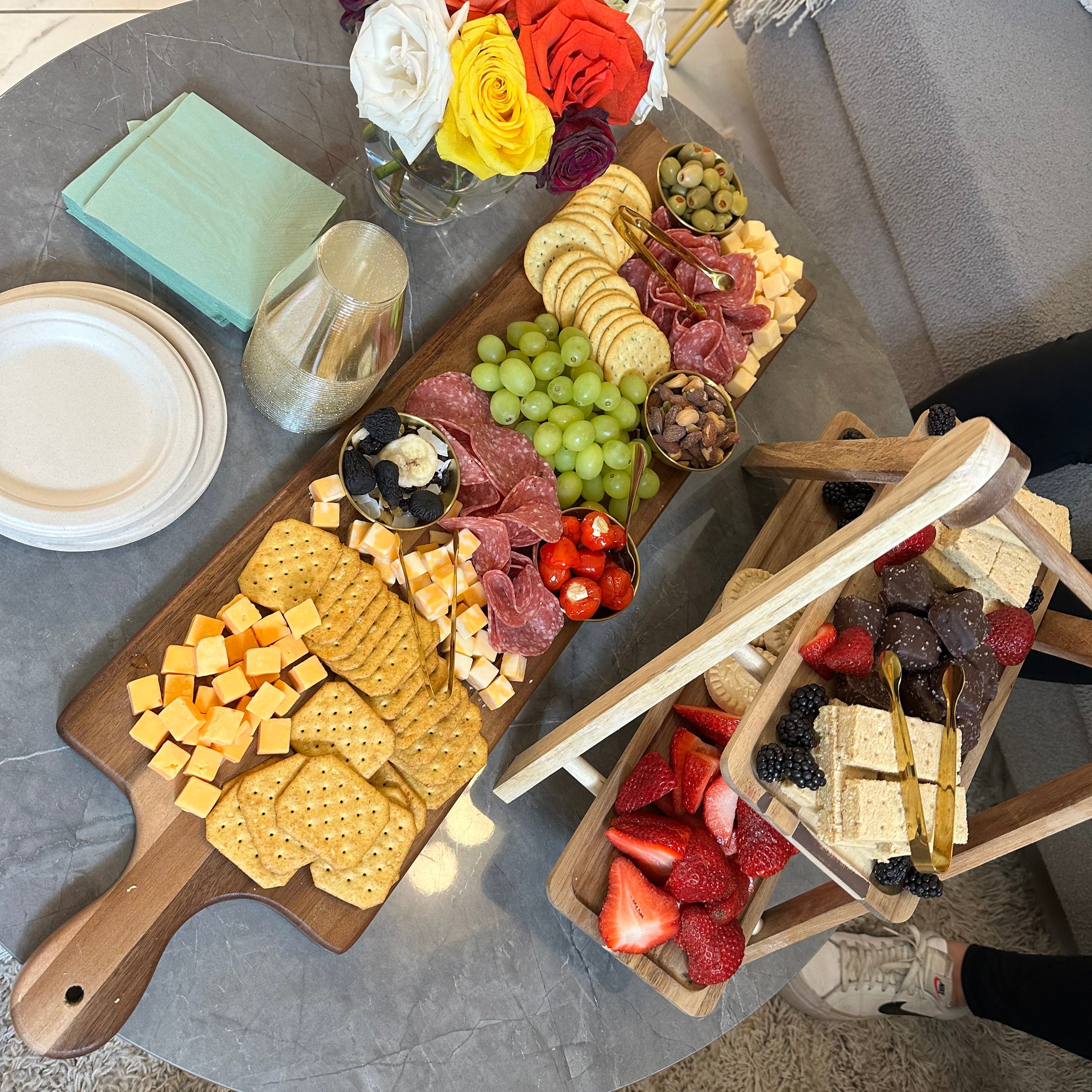 Dessert platter with fruits, cookies, and flowers on a wooden board.