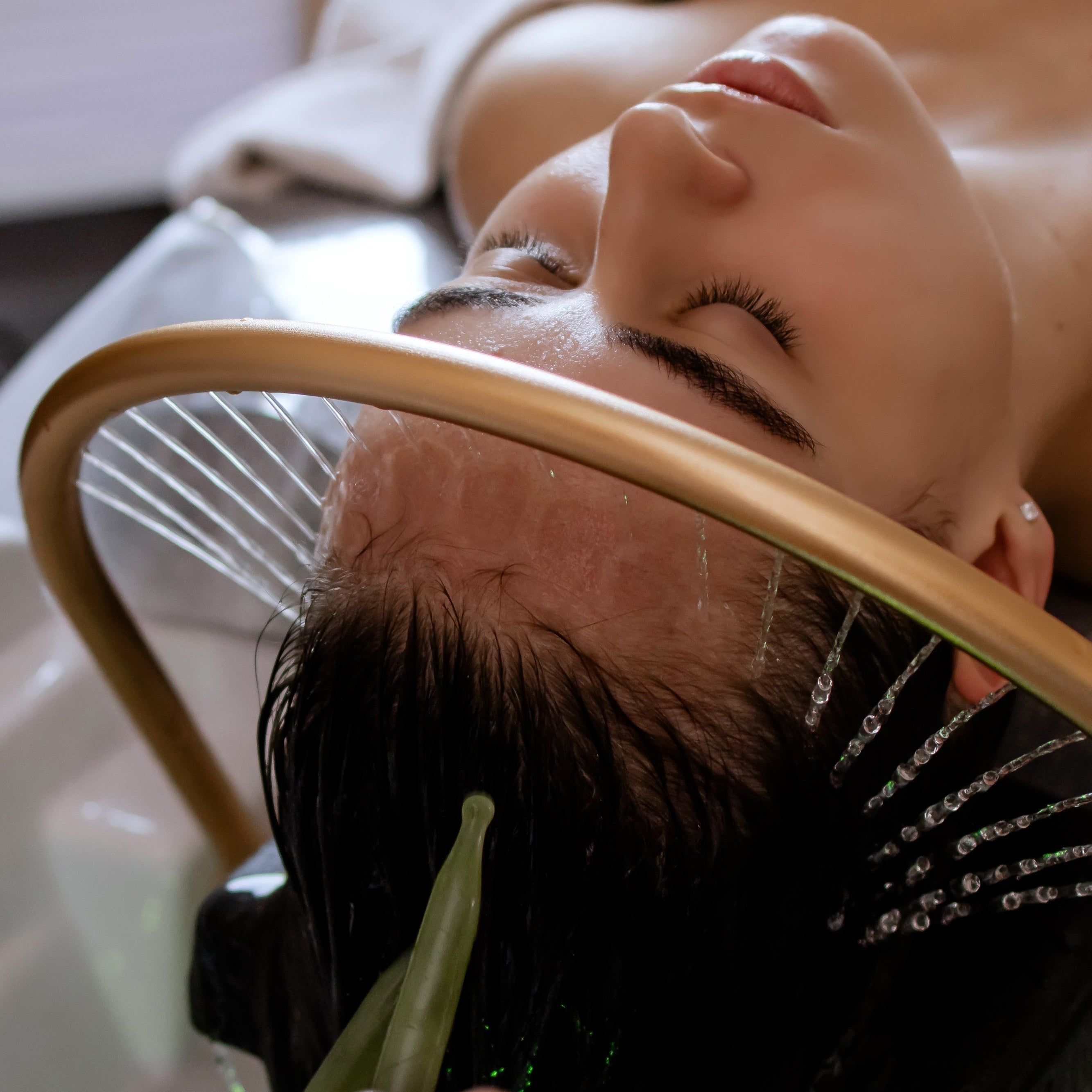 Woman receiving a hair treatment with a brush and green towel in a spa setting