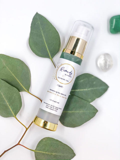 Skincare bottle with gold cap and white label on green leaves and pearls
