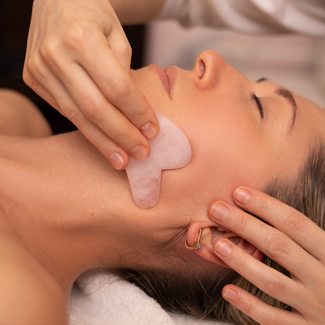 Person receiving a facial treatment with a jade roller on the face.